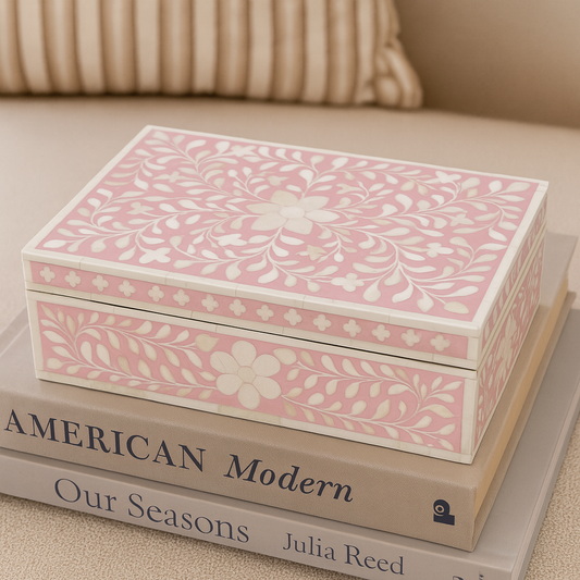 Pink floral-patterned jewelry box on top of books with a beige couch in the background