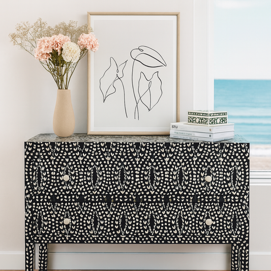 Black and white patterned console table with a vase of flowers and framed artwork in a room.