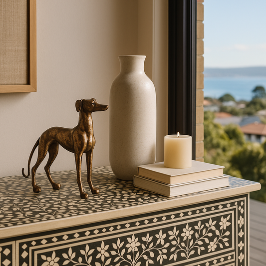Decorative items on a table with a vase, books, and a candle, set against a window view.