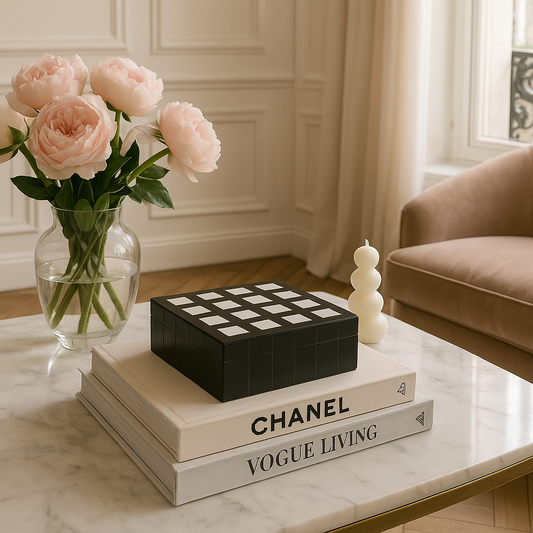Decorative setup with Chanel book, checkered box, and vase of pink roses on a marble surface.