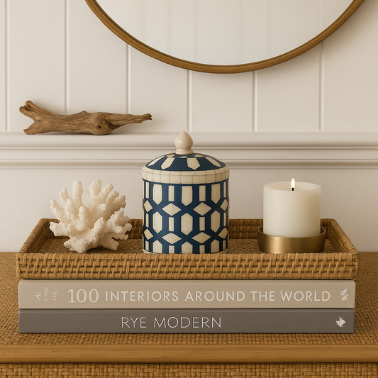 Decorative setup with a blue and white patterned jar, candle, coral sculpture, and books on a wooden surface.