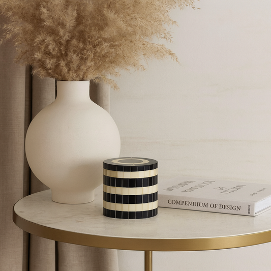 Decorative items on a round marble table with a vase, striped candle, and books.