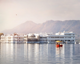Lake Palace hotel on Lake Pichola with a boat and mountains in the background Lake Palace hotel on Lake Pichola with a boat and mountains in the background