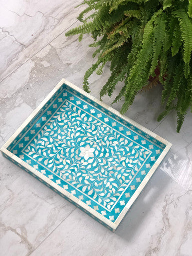 A rectangular decorative tray with a floral bone inlay design in turquoise color, displayed on a marble surface with a green fern in the background.