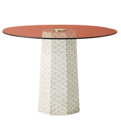 A round dining table with a glass top and a white leg featuring a geometric bone inlay design.