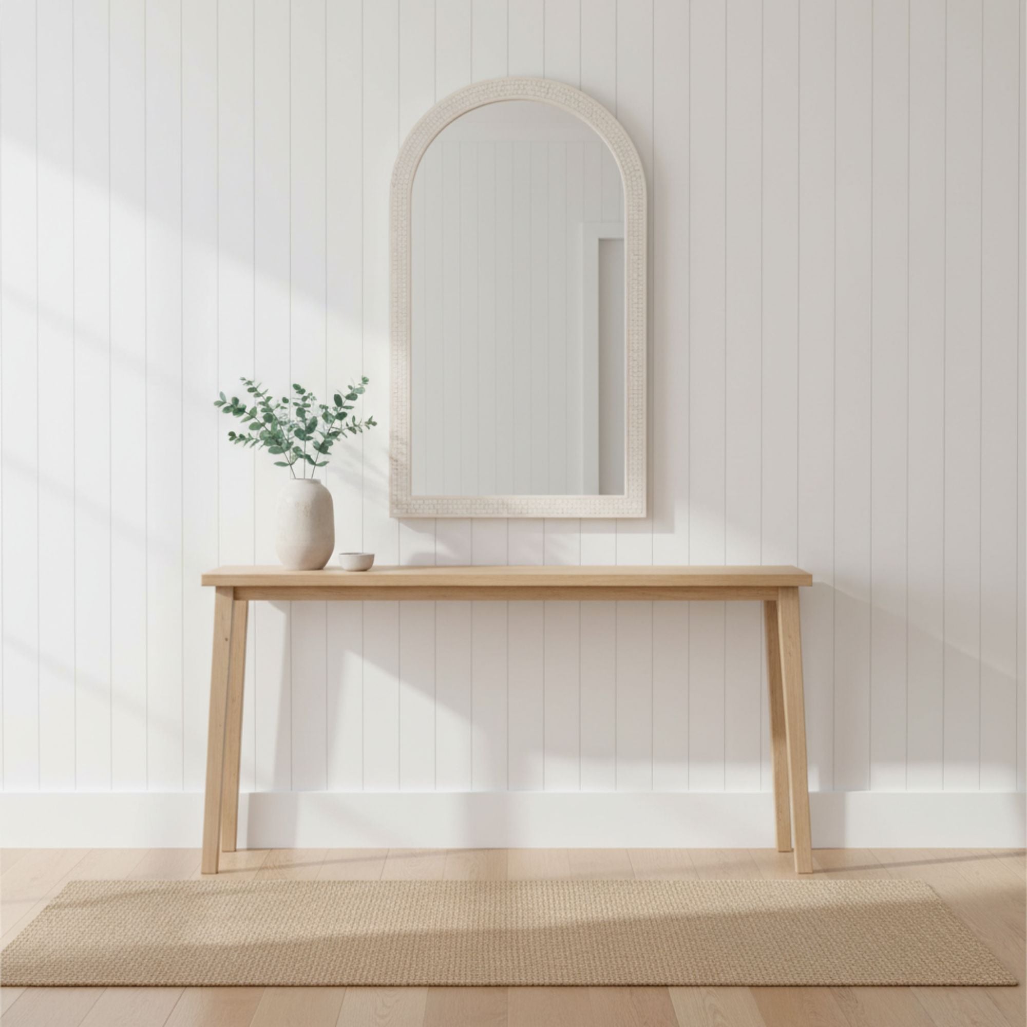 Wooden console table with mirror and plant against a white paneled wall.