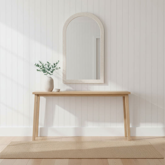 Wooden console table with mirror and plant against a white paneled wall.