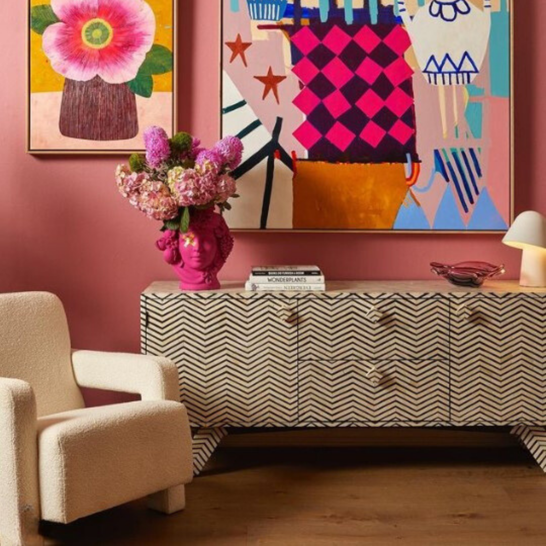 Living room with a pink wall, colorful abstract art, and a patterned sideboard.