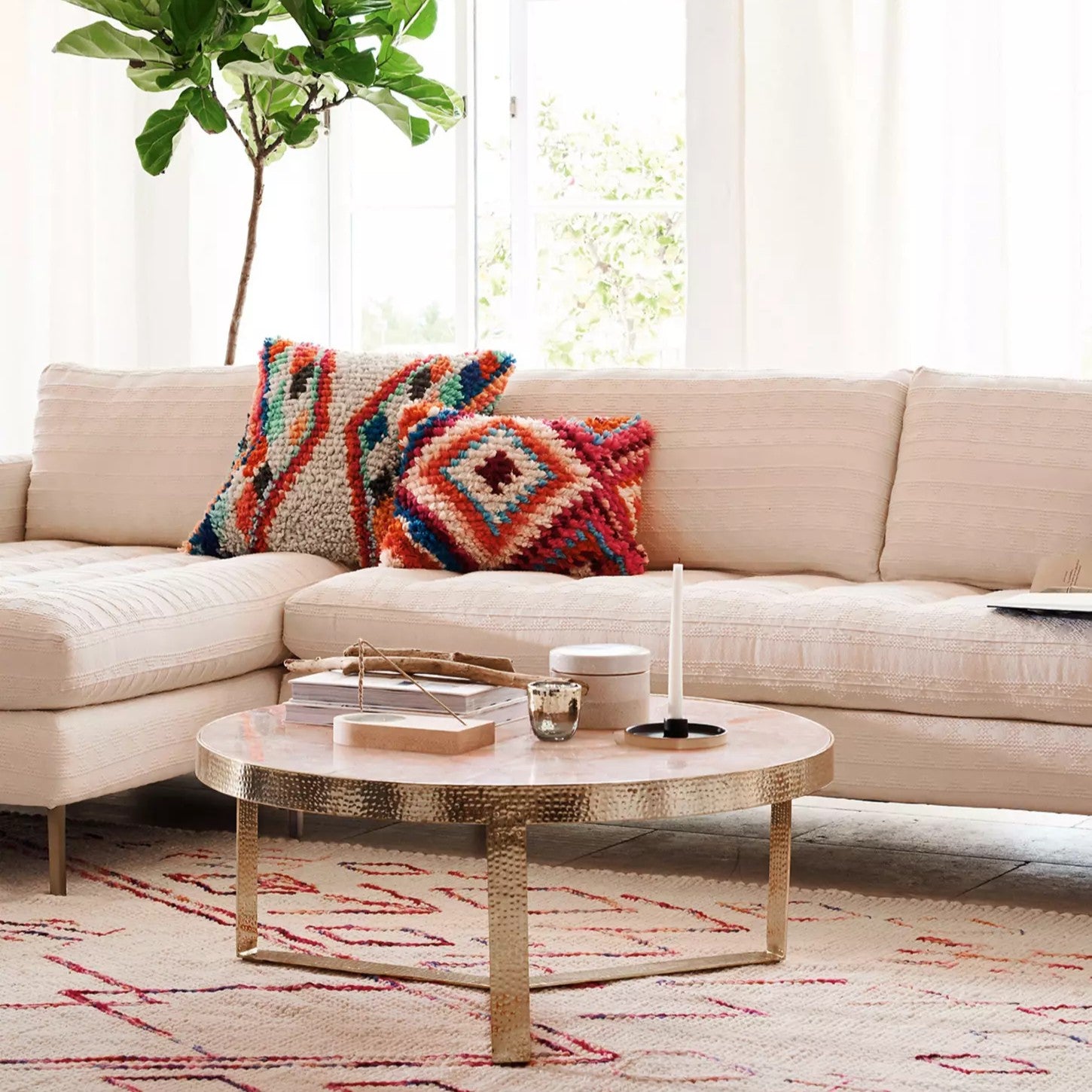Beige sectional sofa with colorful pillows and a round coffee table in a living room setting.