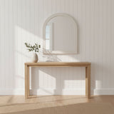 Wooden console table with a mirror and vase against a white paneled wall.