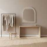 Minimalist interior with a mirror, clothing rack, and table against a beige wall.