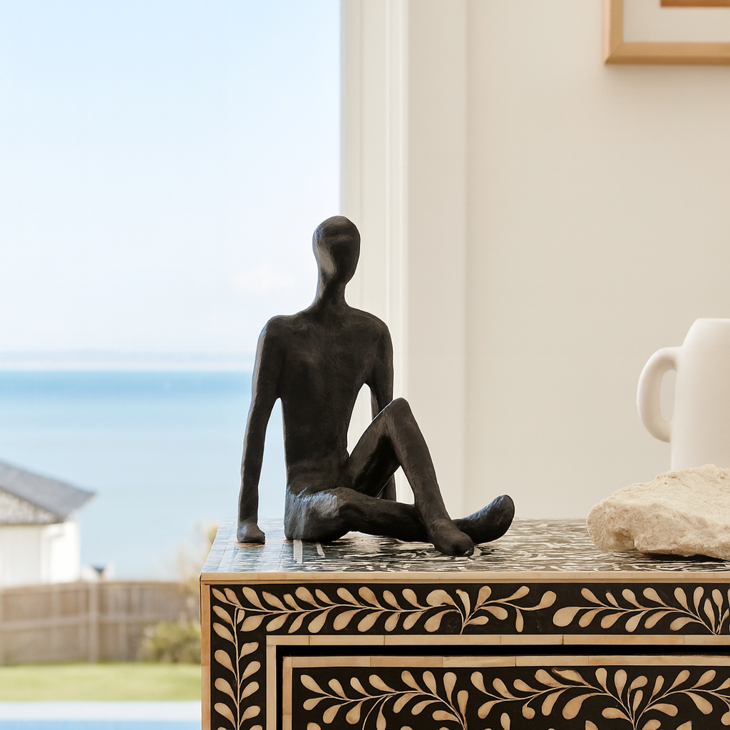 Decorative statue of a sitting figure on a table with a scenic view in the background