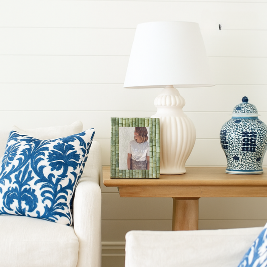Decorative lamp and vase on a wooden side table with a blue and white patterned pillow.