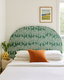 Bedroom with a green patterned headboard, white bedding, and orange pillow.