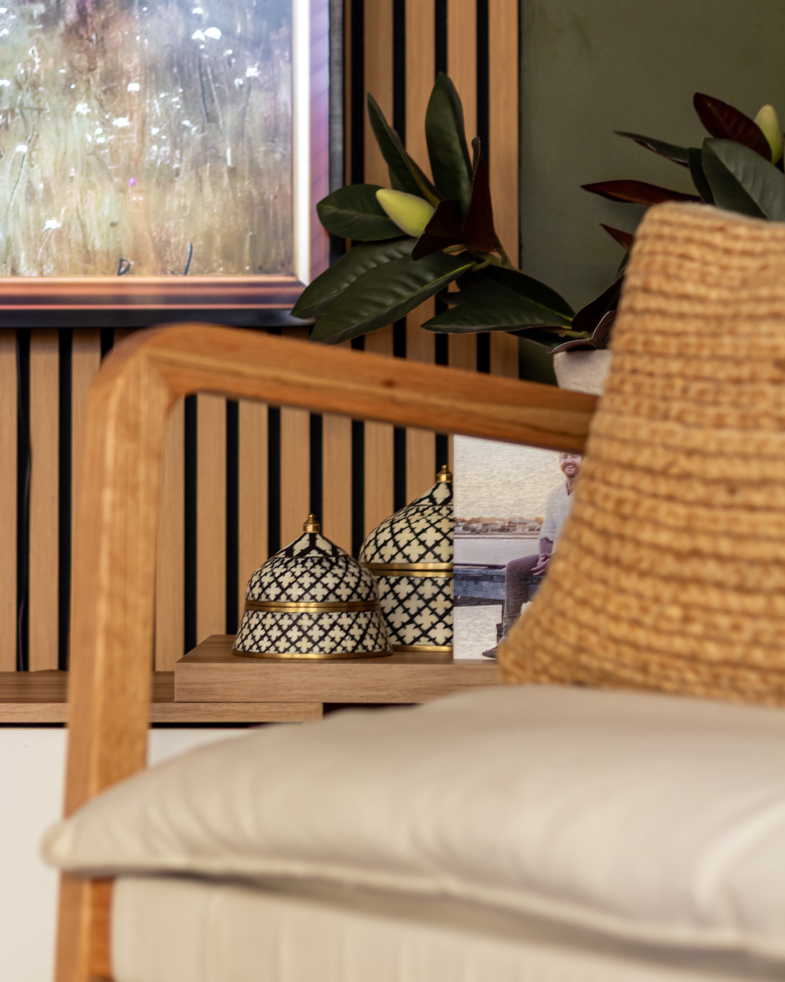 Close-up of a wooden armchair with a woven backrest and white cushion, featuring decorative items on a side table.
