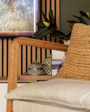 Close-up of a wooden armchair with a woven backrest and white cushion, featuring decorative items on a side table.
