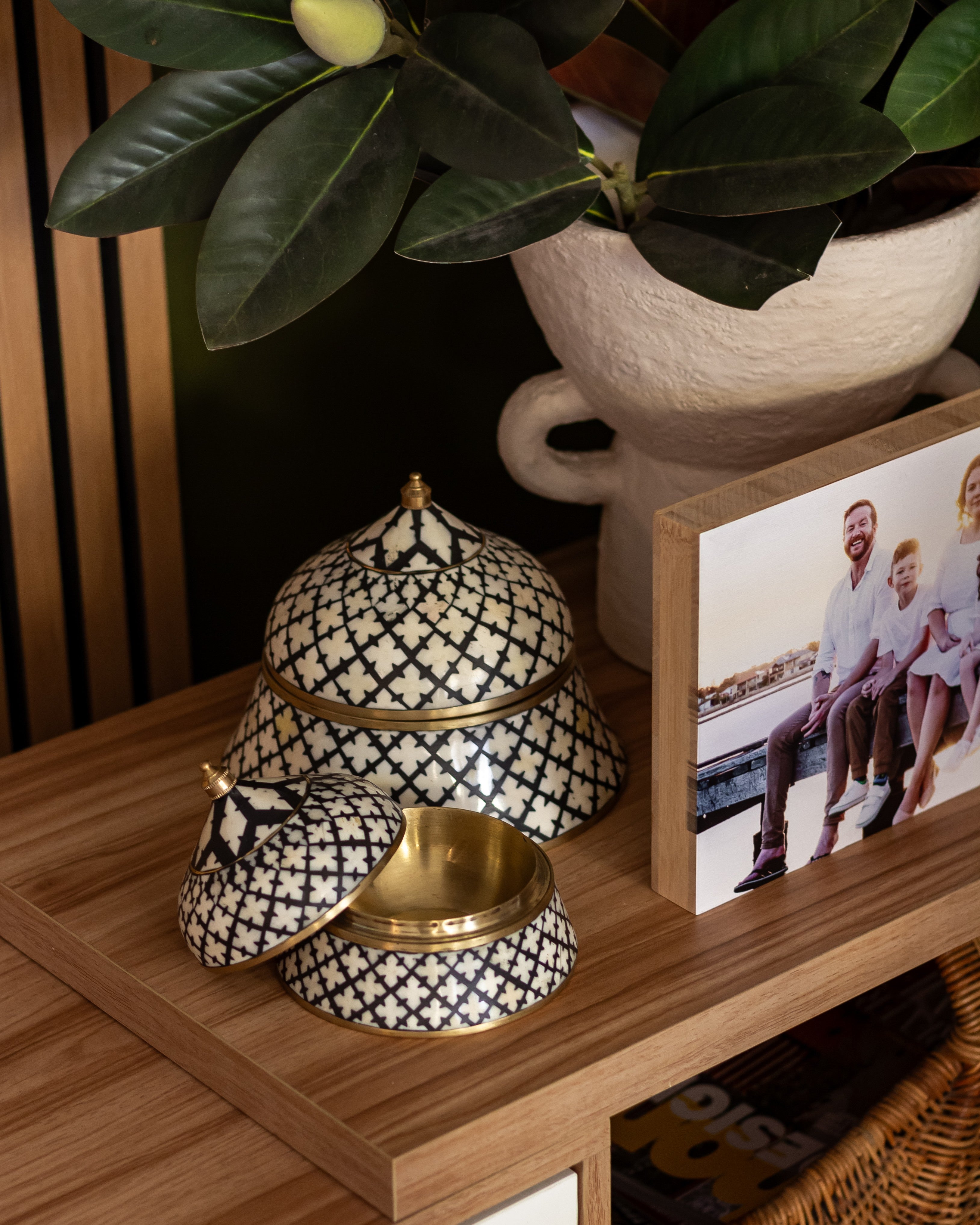 Decorative black and white patterned containers on a wooden surface with a family photo in the background.