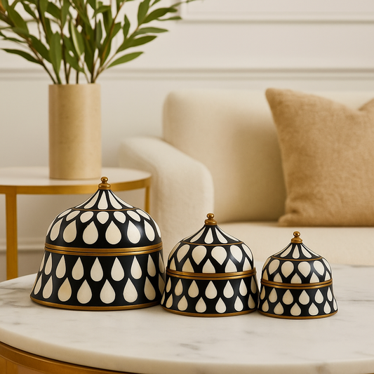 Three black and white patterned ceramic lids on a marble surface with a blurred living room background.