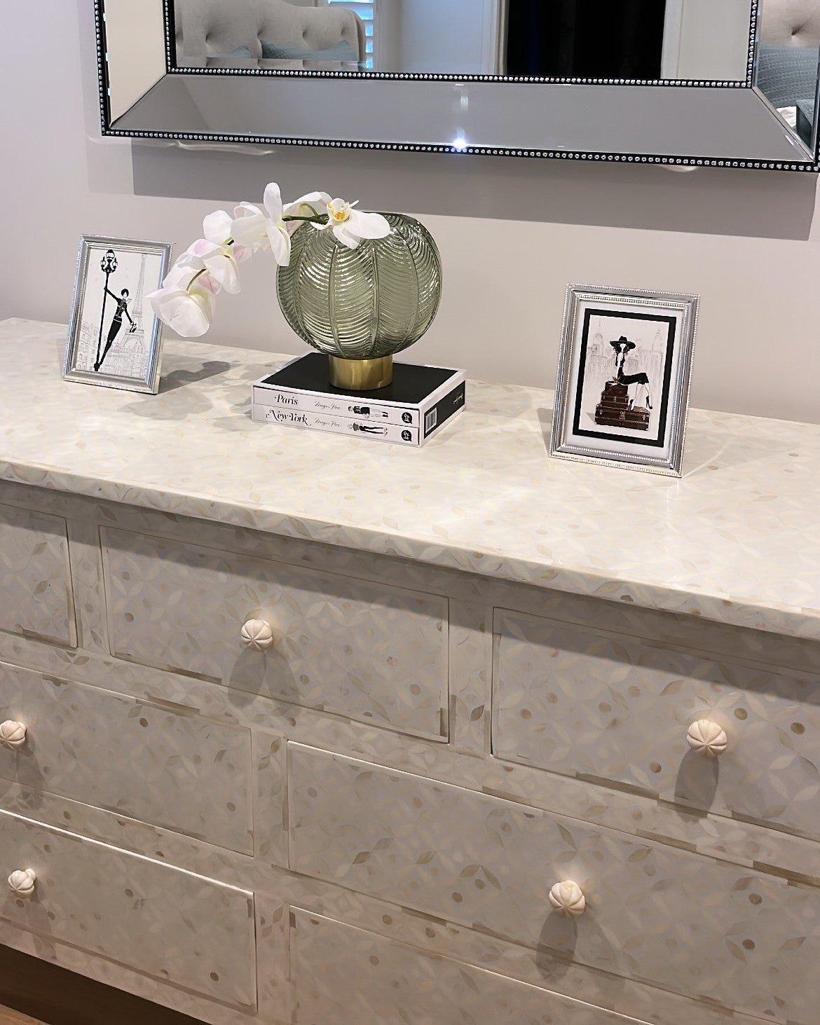 Decorative dresser with a vase, orchids, and framed pictures on top.