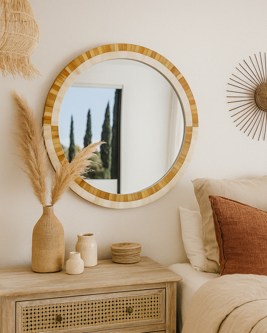 Round mirror with wooden frame on a wall above a wooden nightstand with decorative items.