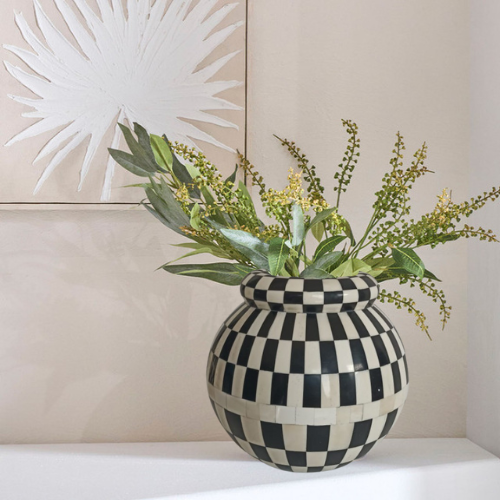 Black and white checkered vase with greenery against a neutral wall


