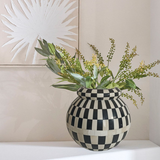 Black and white checkered vase with greenery against a neutral wall

