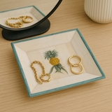 Jewelry dish with gold rings and a pineapple design on a wooden surface