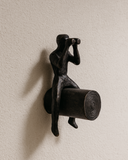 Decorative wall hook shaped like a person with binoculars on a beige wall.
