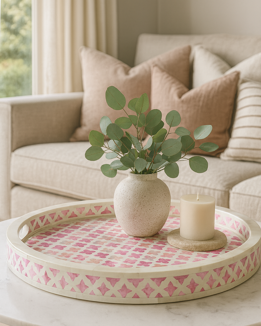 Decorative tray with a vase of greenery and a candle on a coffee table in a living room.