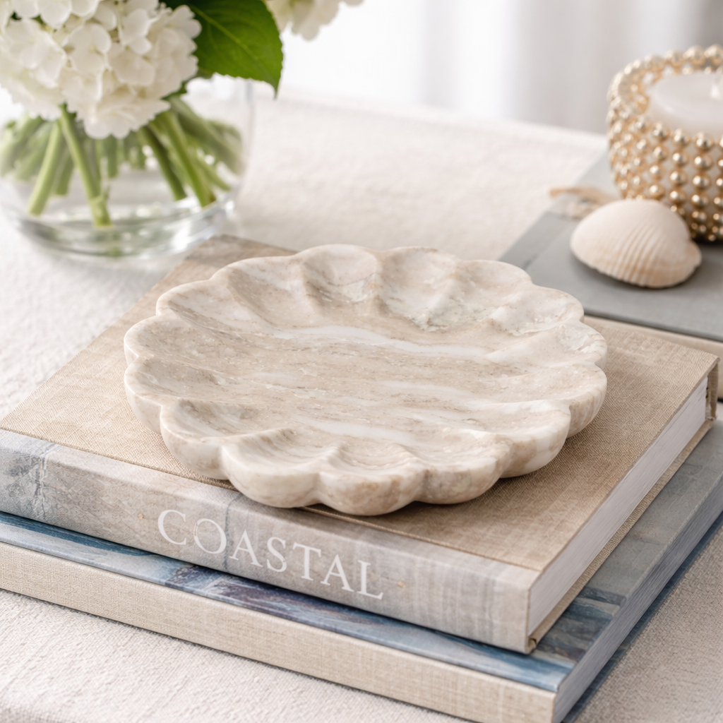 Marble shell-shaped dish on a book titled 'Coastal' with flowers and shells in the background.