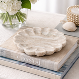 Marble shell-shaped dish on a book titled 'Coastal' with flowers and shells in the background.