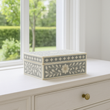 Decorative box with floral patterns on a white surface near a window with greenery outside