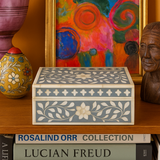Decorative box with floral patterns on a shelf with a colorful painting and other items.