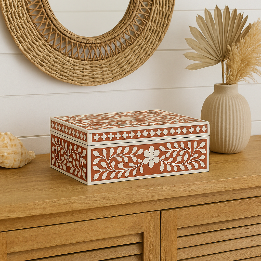 Decorative box with floral patterns on a wooden surface with a vase and shell in the background.