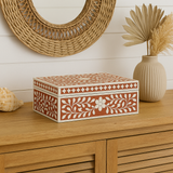 Decorative box with floral patterns on a wooden surface with a vase and shell in the background.