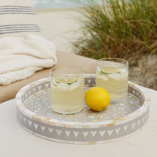 Two glasses of lemonade with lime slices on a decorative tray outdoors.