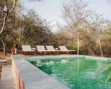 Pool area with lounge chairs and a person in a forest setting