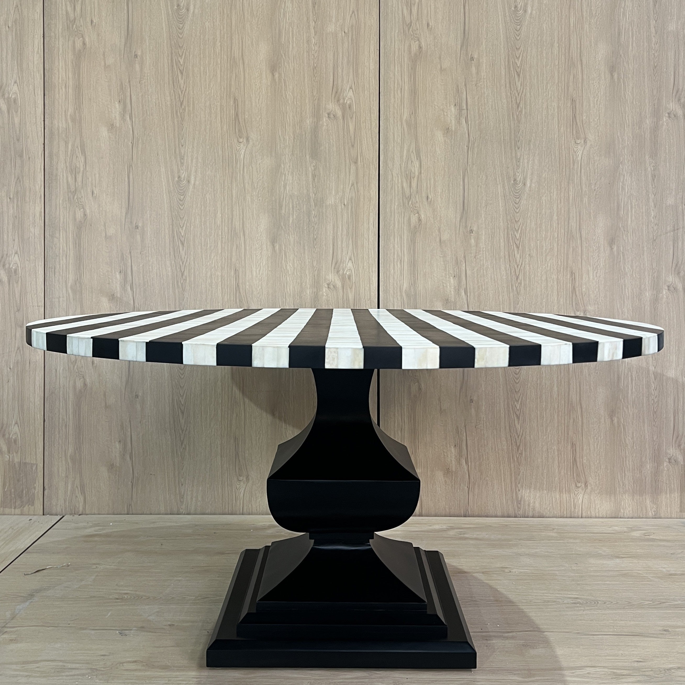 Black and white striped table with a black base on a wooden floor and wall.
