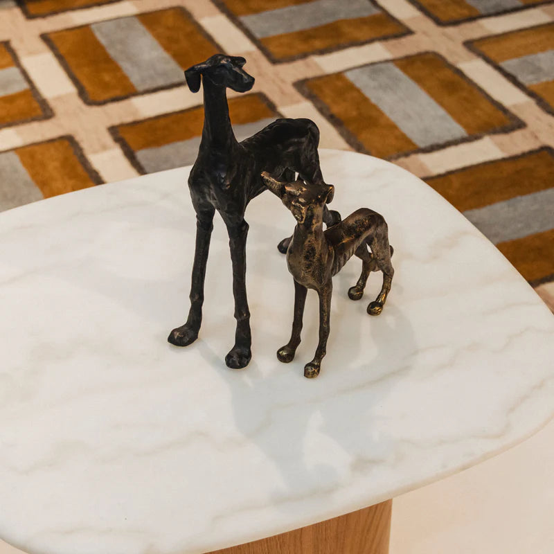 Bronze statues of two dogs on a marble surface with a patterned rug in the background