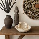 Decorative items including a vase, statue, and woven basket on a wooden table with a wall hanging in the background.