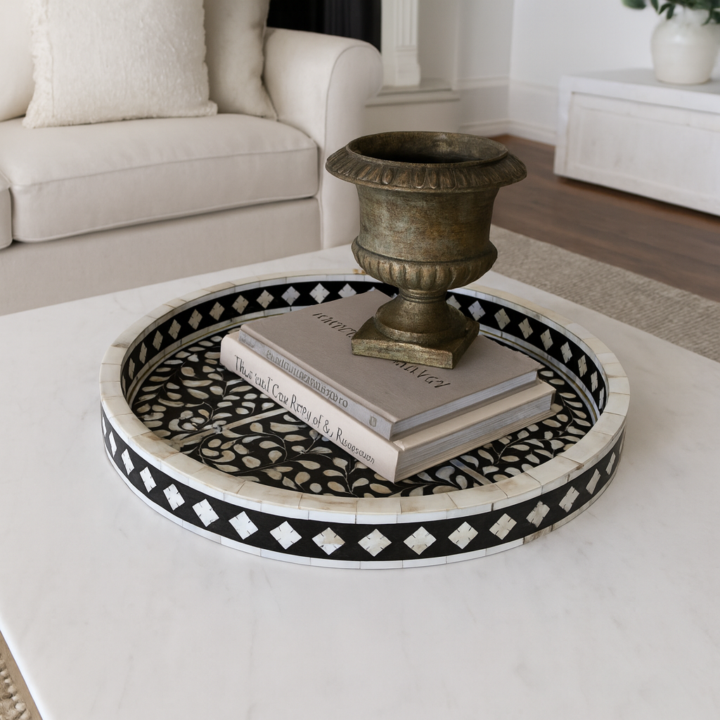Decorative round table with black and white pattern, books, and a decorative urn in a living room setting.