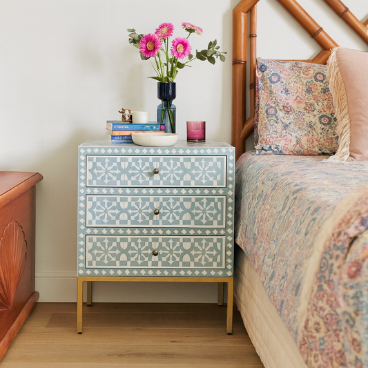 Patterned nightstand with decorative items next to a bed with floral bedding.