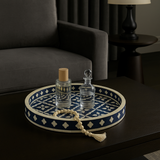 Decorative tray with two glass bottles on a dark surface, with a gray sofa and lamp in the background.