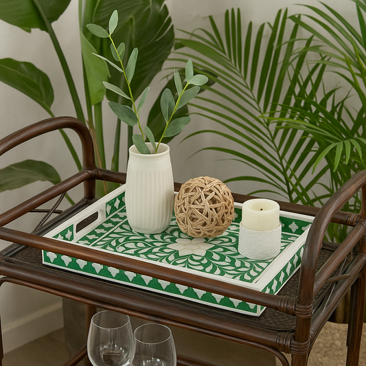 Decorative tray with a vase, candle, and decorative ball on a wooden cart with plants in the background.