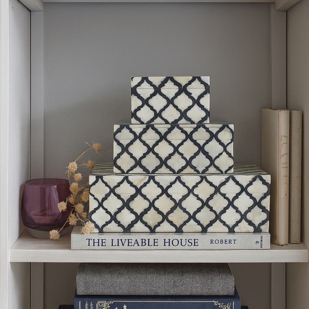 Decorative boxes with a geometric pattern on a shelf with books and a vase.