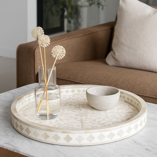 Decorative tray with a vase and flowers on a marble surface, with a couch in the background.