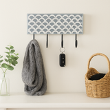 Wall-mounted hook rack with decorative pattern, holding a scarf, keys, and a basket.