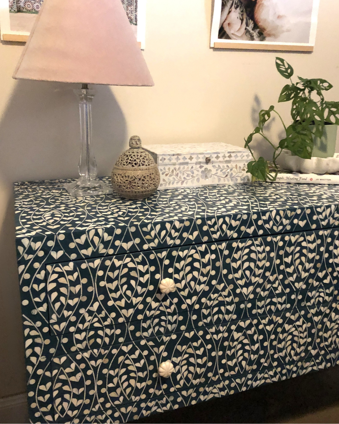 Cabinet with a patterned cover, lamp, and plant in a room setting.