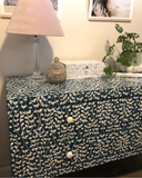 Cabinet with a patterned cover, lamp, and plant in a room setting.
