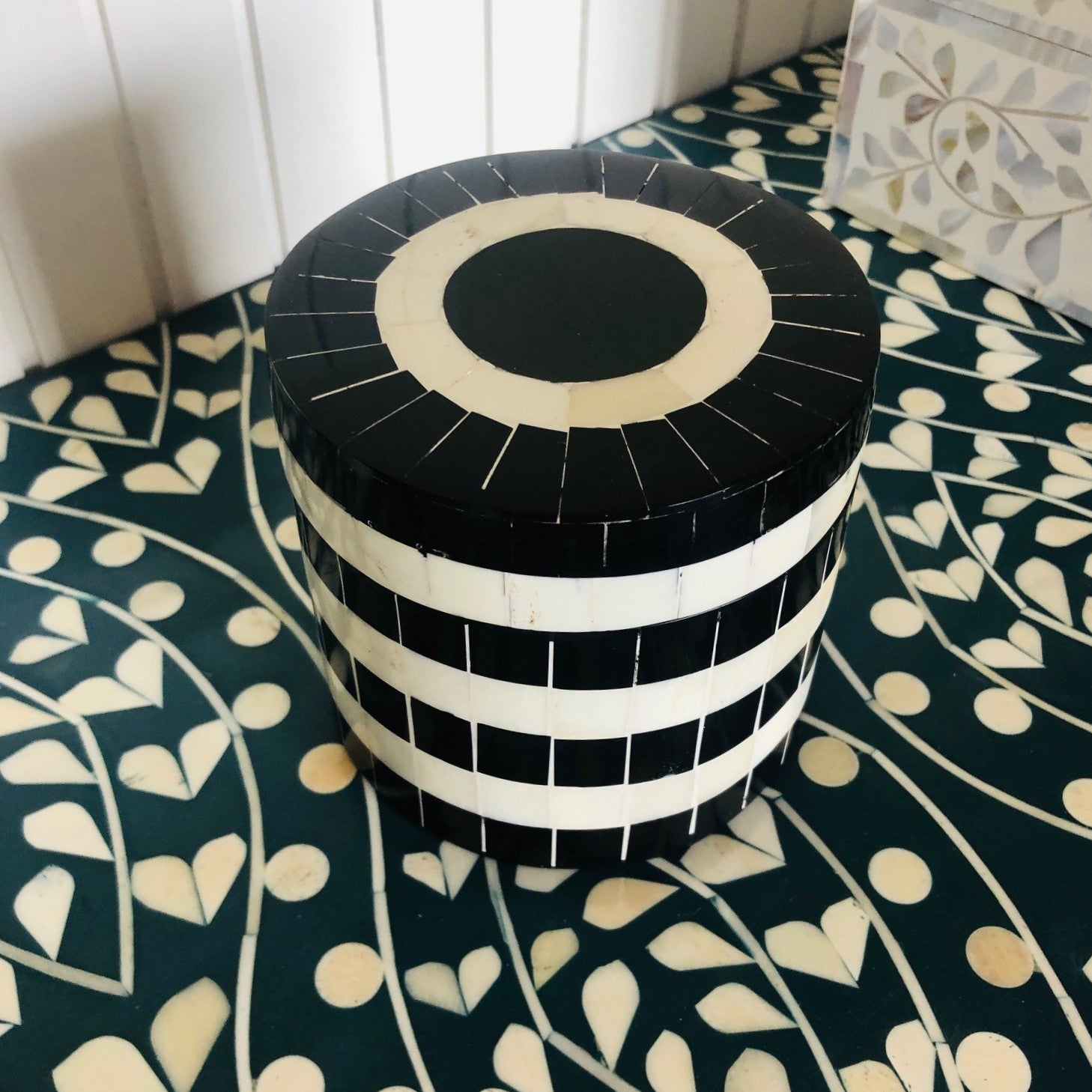 Black and white striped cylindrical container on a patterned surface